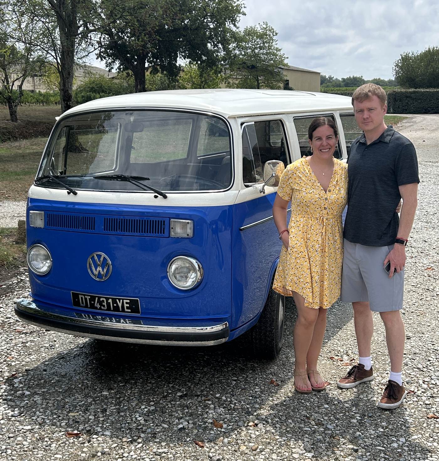 Standing beside a blue VW bus on a gravel drive